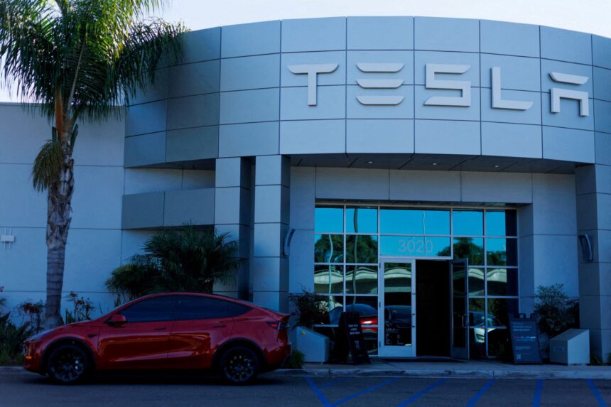 Fachada de uma concessionária Tesla com um carro elétrico vermelho estacionado em frente, ao lado de uma palmeira.