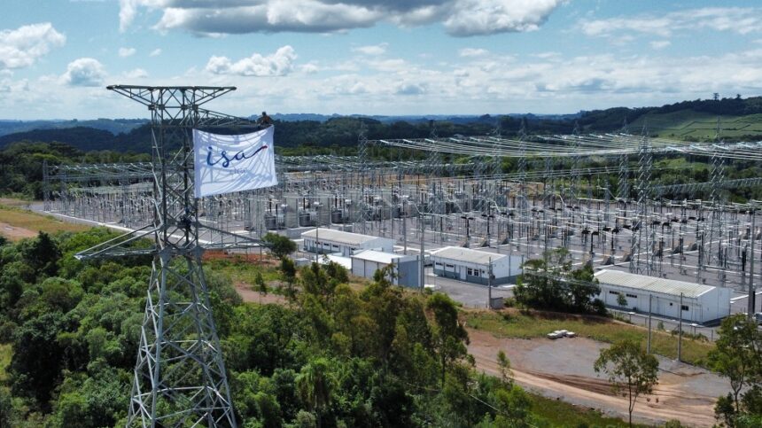 Torres de transmissão elétrica em subestação cercada por vegetação. Pessoa no topo de torre instala bandeira branca.