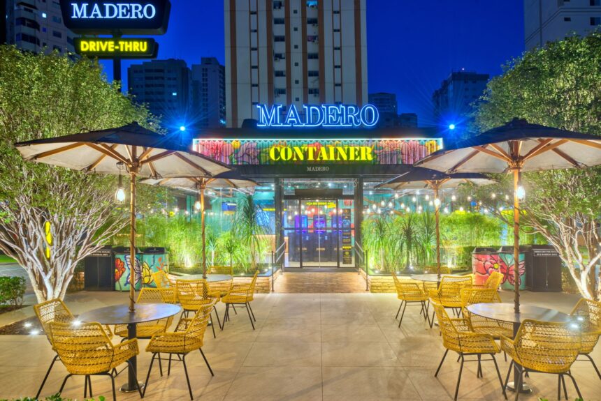 Restaurante Madero ao anoitecer, com mesas externas vazias, guarda-sóis abertos e decoração de luzes e vegetação.