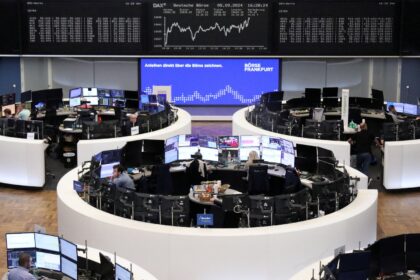 Corretoras monitoram telas em uma movimentada bolsa de valores, com gráficos de ações e dados financeiros ao fundo.
