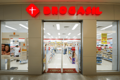 Entrada de uma farmácia Drogasil iluminada, com prateleiras organizadas e cartazes de promoções visíveis ao fundo.