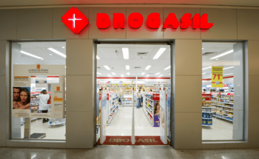 Entrada de uma farmácia Drogasil iluminada, com prateleiras organizadas e cartazes de promoções visíveis ao fundo.