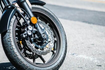 Roda dianteira de moto esportiva com disco de freio destacado, estacionada em rua asfaltada.