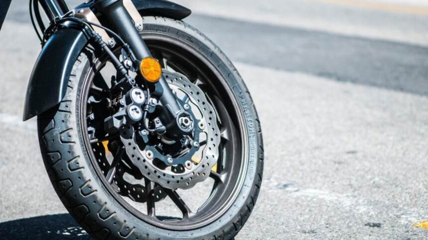 Roda dianteira de moto esportiva com disco de freio destacado, estacionada em rua asfaltada.