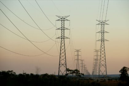 Torres de transmissão de energia ao pôr do sol, destacando infraestrutura elétrica em paisagem rural.