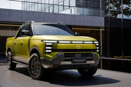 Picape híbrida Nissan Frontier Pro verde, com design robusto, diante de edifício moderno de vidro e concreto.