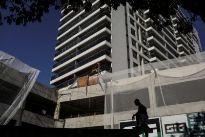 Edifício moderno em construção com silhueta de trabalhador em destaque. Estrutura de concreto e andares com varandas.