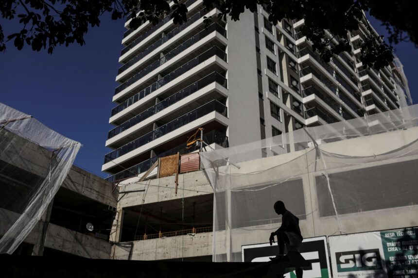 Edifício moderno em construção com silhueta de trabalhador em destaque. Estrutura de concreto e andares com varandas.