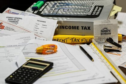 Documentos fiscais e materiais de escritório em uma mesa, com uma calculadora, livros de imposto de renda e faturas.