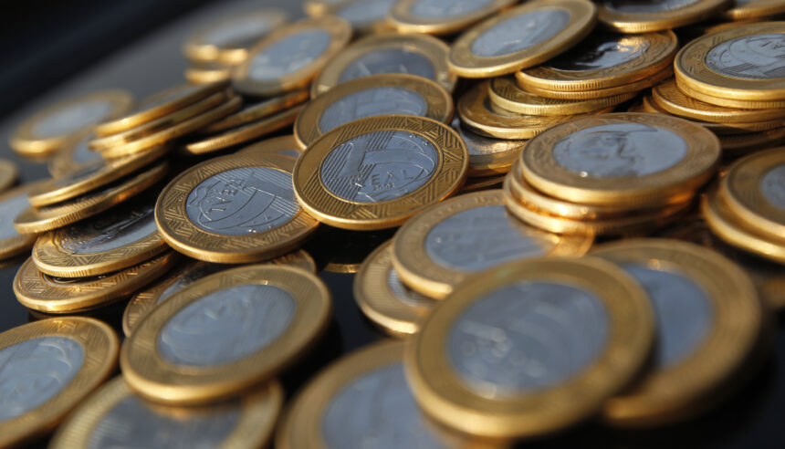 Moedas de real espalhadas, destacando detalhes dourados e prateados, simbolizando economia e finanças no Brasil.