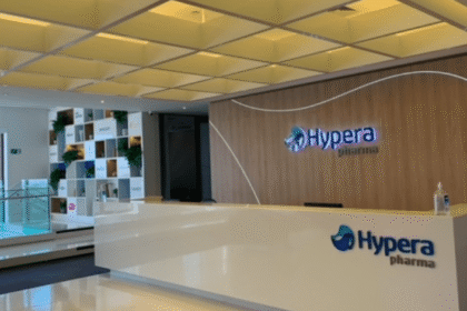 Recepção moderna da Hypera Pharma, com balcão branco, logotipo na parede de madeira e estante decorativa ao fundo.