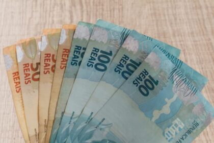 Mãos segurando diversas notas de real, incluindo cédulas de 100 e 50, representando economia e finanças no Brasil.