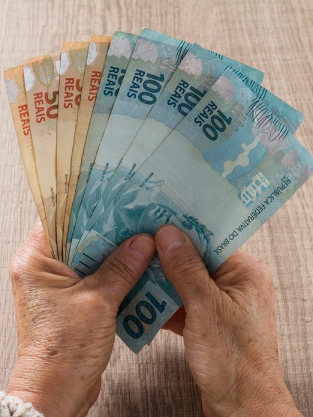 Mãos segurando diversas notas de real, incluindo cédulas de 100 e 50, representando economia e finanças no Brasil.