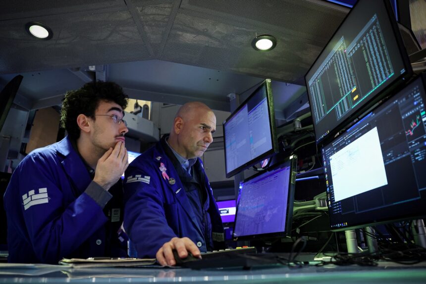 Dois operadores de mercado analisam gráficos financeiros em múltiplos monitores, focando em decisões de investimento.