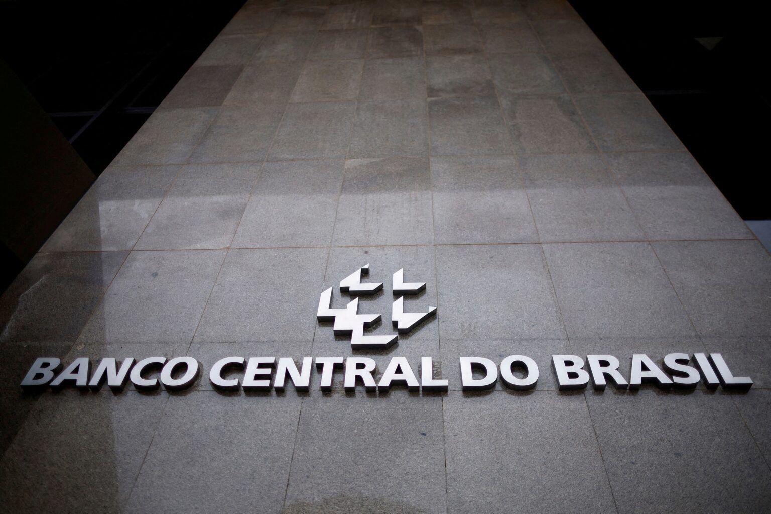 Fachada do Banco Central do Brasil em Brasília, destacando o logotipo e letras em metal brilhante sobre superfície de pedra.