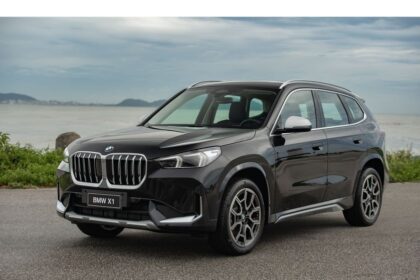 SUV BMW X1 preto estacionado à beira-mar, destacando design elegante e modernidade em cenário costeiro.