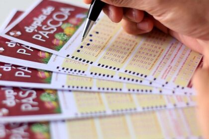 Pessoa marca números em bilhetes da Dupla de Páscoa, destacando a expectativa de participar do sorteio especial.