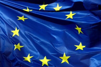 Bandeira da União Europeia tremulando, destacando estrelas amarelas sobre fundo azul, símbolo de unidade e cooperação.