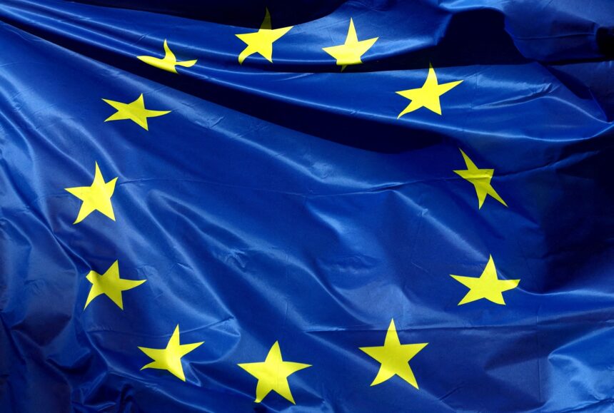 Bandeira da União Europeia tremulando, destacando estrelas amarelas sobre fundo azul, símbolo de unidade e cooperação.