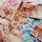 Notas de reais brasileiras de diferentes valores espalhadas, destacando as cédulas de 50 e 100 reais.