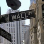 Placa de rua de Wall Street em destaque, cercada por prédios altos, simbolizando o centro financeiro de Nova York.