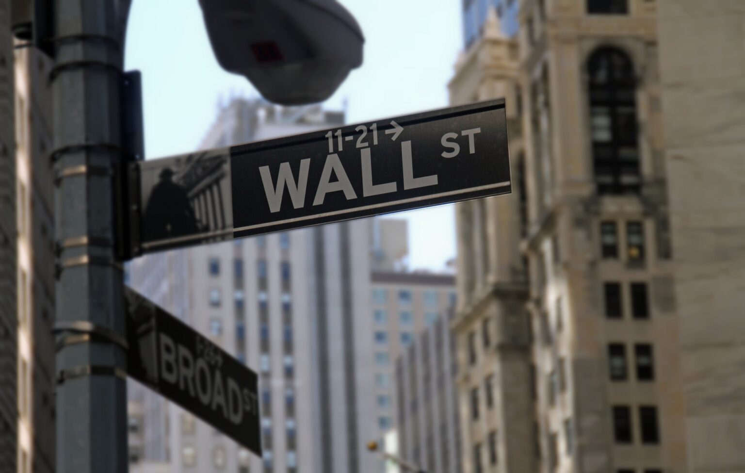 Placa de rua de Wall Street em destaque, cercada por prédios altos, simbolizando o centro financeiro de Nova York.