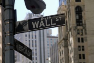 Placa de rua de Wall Street em destaque, cercada por prédios altos, simbolizando o centro financeiro de Nova York.
