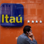 Homem caminha ao telefone em frente a uma agência do Itaú, destacando logo do banco e fachada laranja com estrelas.