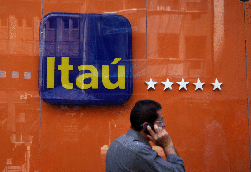 Homem caminha ao telefone em frente a uma agência do Itaú, destacando logo do banco e fachada laranja com estrelas.