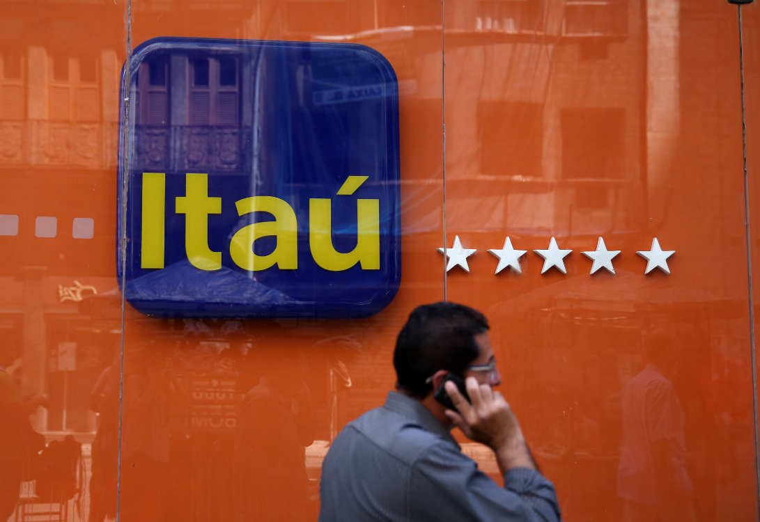 Homem caminha ao telefone em frente a uma agência do Itaú, destacando logo do banco e fachada laranja com estrelas.