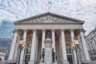 Fachada do Royal Exchange em Londres com colunas neoclássicas, esculturas, lâmpadas e céu nublado ao fundo.