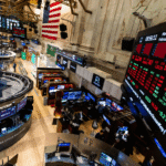 Corretoras trabalham no movimentado piso da Bolsa de Valores de Nova York, com gráficos de ações em grandes monitores.