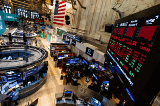 Corretoras trabalham no movimentado piso da Bolsa de Valores de Nova York, com gráficos de ações em grandes monitores.