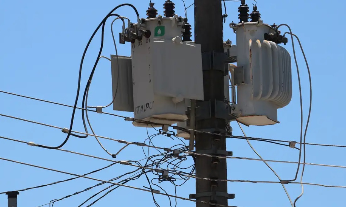 Transformador elétrico em poste, cercado por fios. Equipamento essencial para distribuição de energia elétrica urbana.