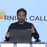 Pessoa apresentando programa financeiro Morning Call em frente a um laptop, gesticulando enquanto discute tendências de mercado.