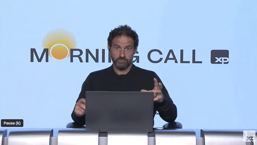 Pessoa apresentando programa financeiro Morning Call em frente a um laptop, gesticulando enquanto discute tendências de mercado.