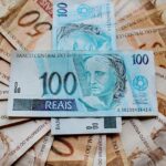 Notas de real brasileiro espalhadas, com destaque para cédulas de 50 e 100 reais, simbolizando economia e finanças.