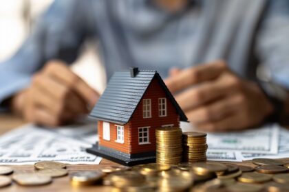 Miniatura de casa cercada por moedas empilhadas, simbolizando investimento imobiliário e finanças pessoais.
