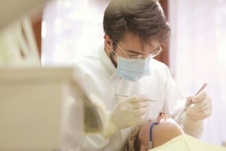 Dentista atendendo paciente em um consultório, usando máscara e luvas, realizando procedimento odontológico com instrumentos.