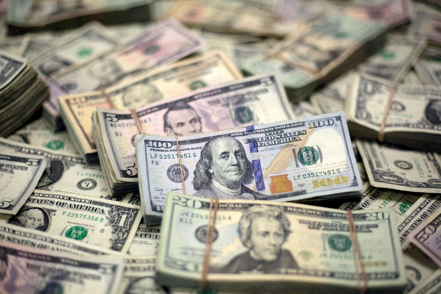 Pilhas de cédulas de dólar americano, destacando notas de 100, 20 e 5 dólares, simbolizando riqueza e finanças.