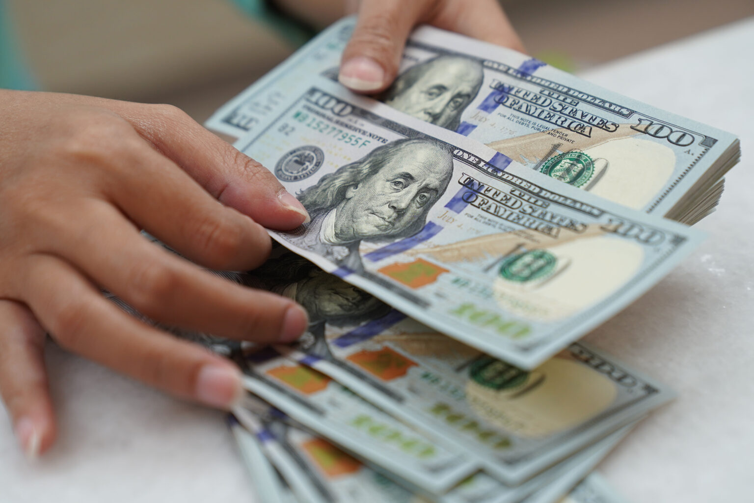 Mãos contando notas de cem dólares, representando finanças pessoais e gestão de dinheiro.