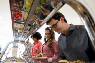 Pessoas servindo-se em buffet de comida variada em restaurante, com pratos coloridos e opções de saladas frescas.