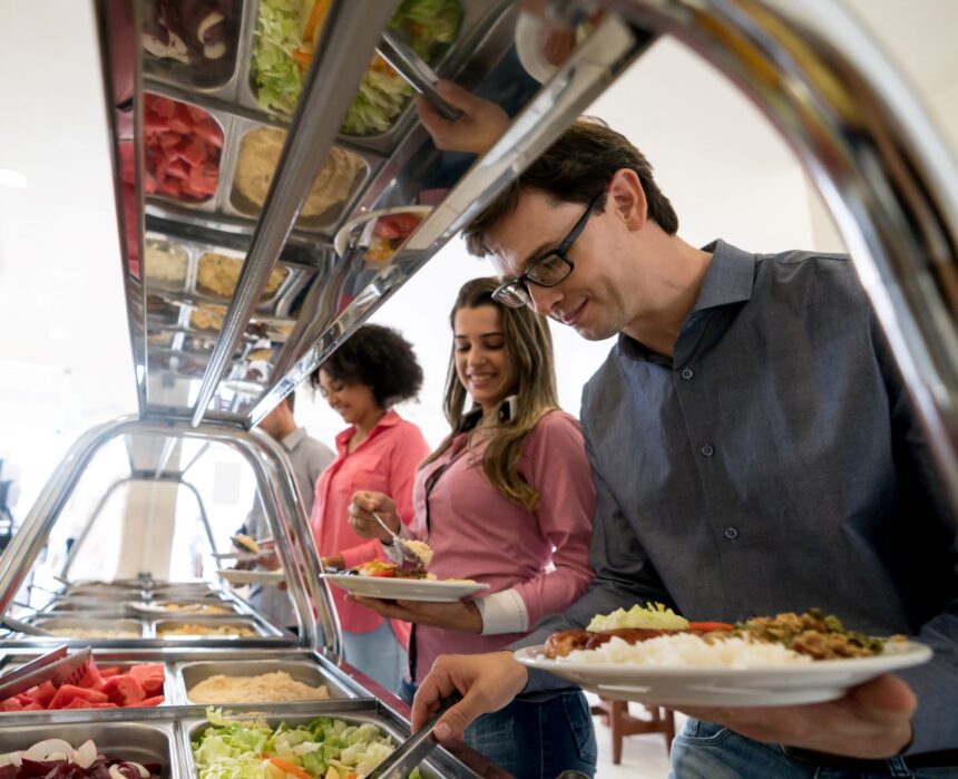 Pessoas servindo-se em buffet de comida variada em restaurante, com pratos coloridos e opções de saladas frescas.