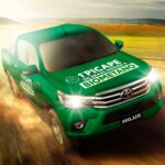 Picape verde movida a biometano acelera em estrada de terra sob céu claro, destacando sustentabilidade automotiva.