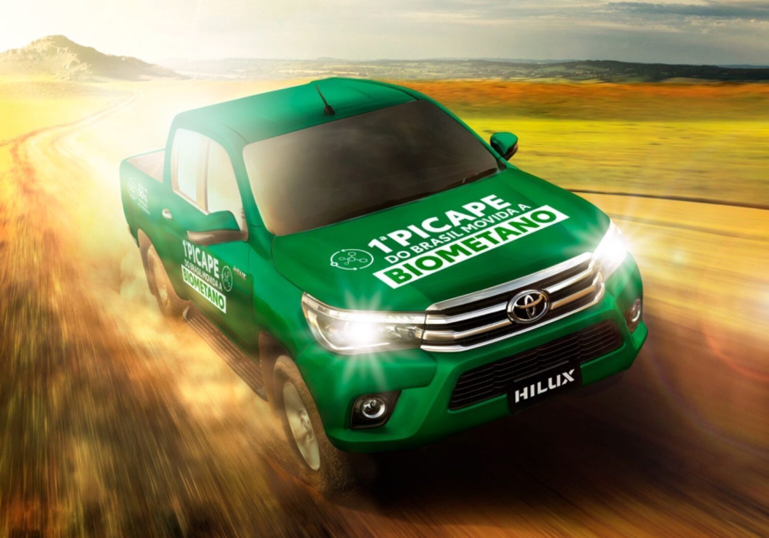 Picape verde movida a biometano acelera em estrada de terra sob céu claro, destacando sustentabilidade automotiva.