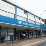 Fachada de prédio da Previdência Social, com pessoas caminhando na calçada e fachada azul destacada pelo nome do órgão.