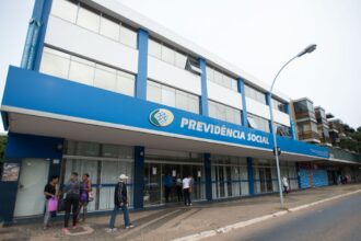 Fachada de prédio da Previdência Social, com pessoas caminhando na calçada e fachada azul destacada pelo nome do órgão.