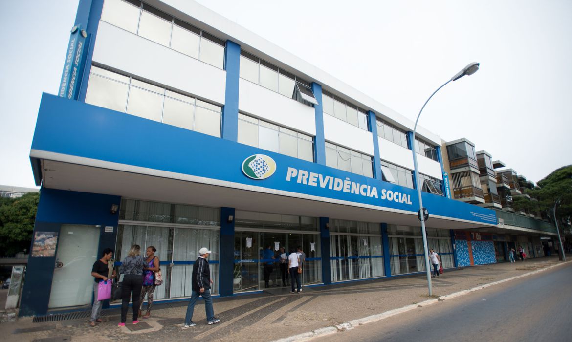 Fachada de prédio da Previdência Social, com pessoas caminhando na calçada e fachada azul destacada pelo nome do órgão.