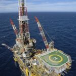 Plataforma de petróleo offshore em mar aberto com heliponto, gruas e estrutura complexa; destaque para exploração marítima.