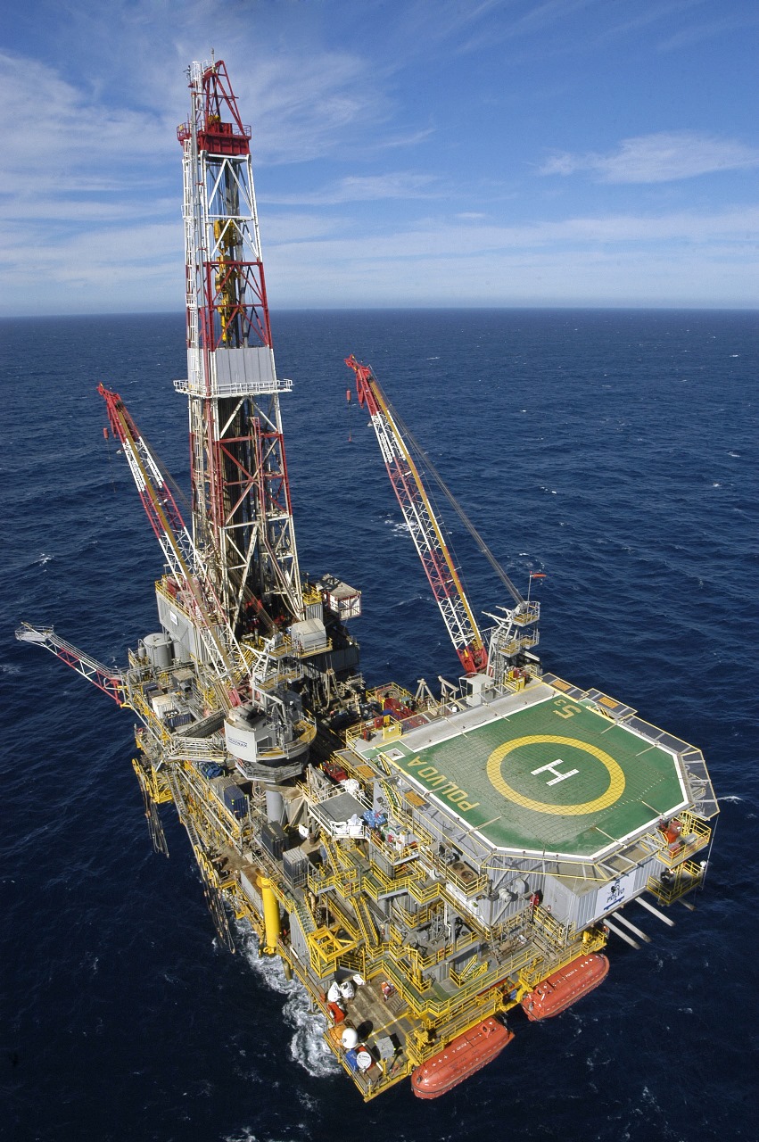 Plataforma de petróleo offshore em mar aberto com heliponto, gruas e estrutura complexa; destaque para exploração marítima.